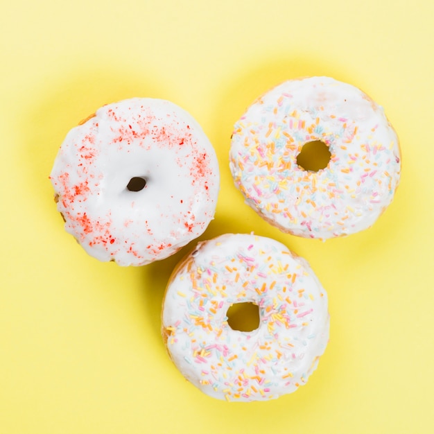 Free photo sweet donuts glazed with sprinkles on yellow background