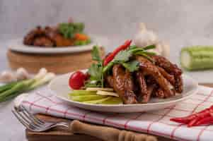 Free photo sweet fried chicken feet in a white plate with coriander, chili, cucumber, and tomato.