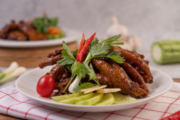 Free photo sweet fried chicken feet in a white plate with coriander, chili, cucumber, and tomato.