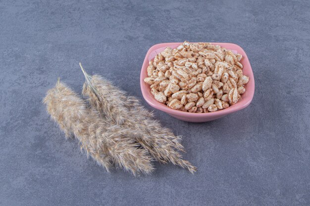 Sweet muesli in a bowl next to pampas grass, on the blue background.