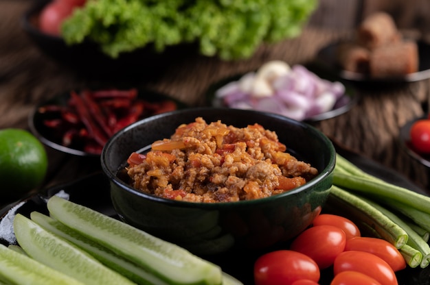 Sweet pork in a black bowl, complete with cucumbers, long beans, tomatoes, and side dishes