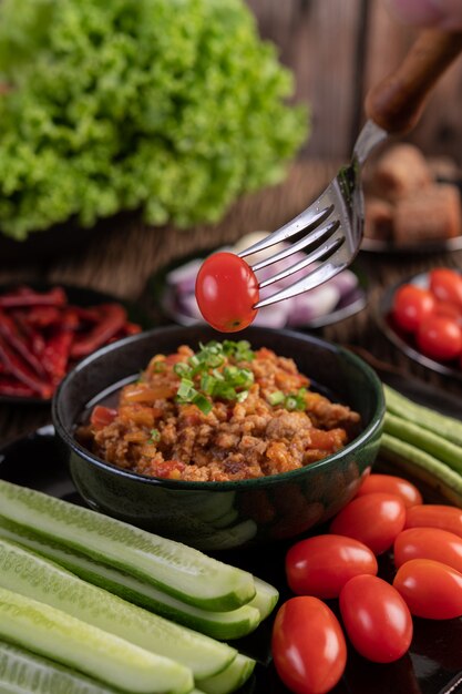 Sweet pork in a black bowl, complete with cucumbers, long beans, tomatoes, and side dishes