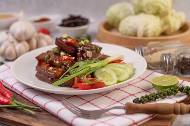 Sweet pork on a white plate with chopped scallions, chili, lime, cucumber, tomato, and garlic.