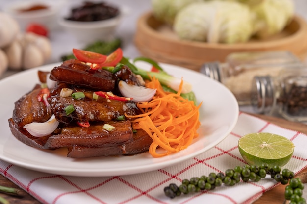 Sweet pork in a white plate with chopped scallions, chili, lime, gourd, tomato and garlic.