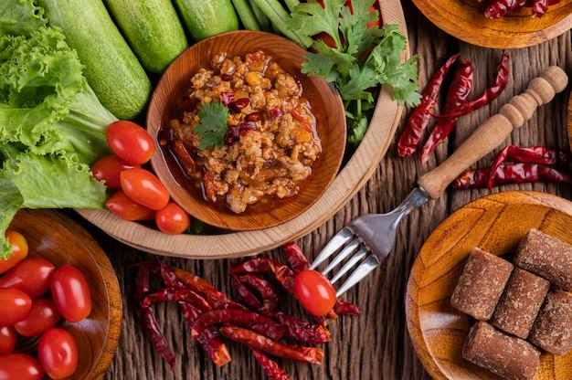 Sweet pork in a wooden bowl with cucumber, long beans, tomatoes, and side dishes.