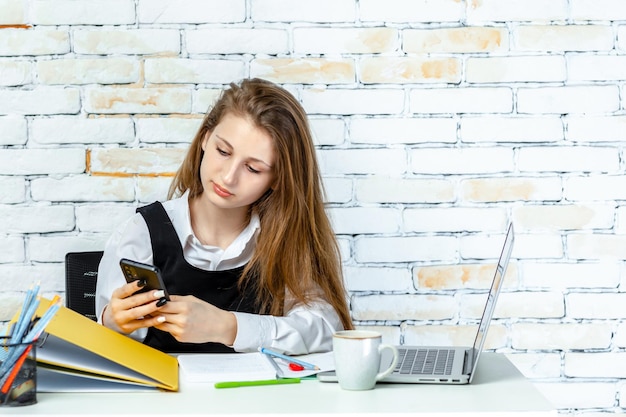 Sweet school girl sitting behind of her desk and playing with her phone