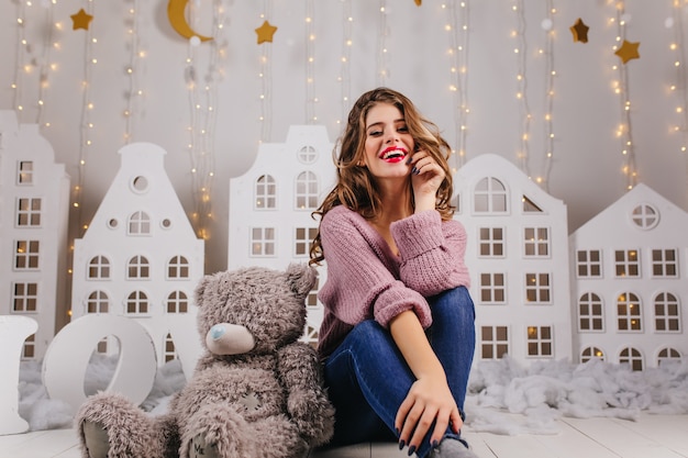 Free photo sweet, smiling, young girl in cozy is sitting on floor with teddy bear