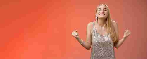 Free photo sweet taste win charming happy blond girl rejoicing triumphing raise head up close eyes smiling broadly clench fists victory celebration gesture achieve dream come true standing red background