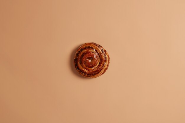 Sweet yummy freshly baked swirling cinnamon bun for your snack or breakfast. Appetizing unhealthy puff cake on beige background. Confectionery and bakery concept. Whole delicious french roll