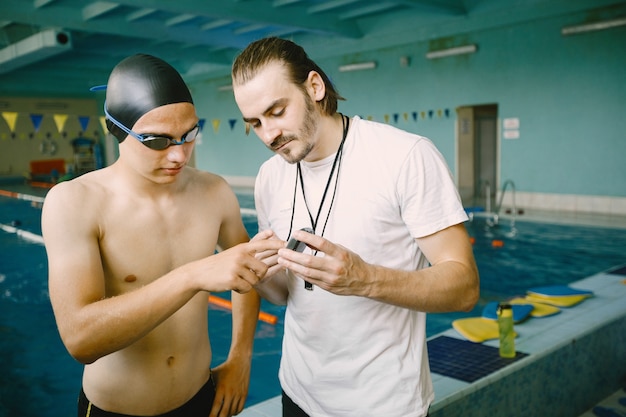 Swimmer and coach discussing by pool. European ethnicity. Leisure center.