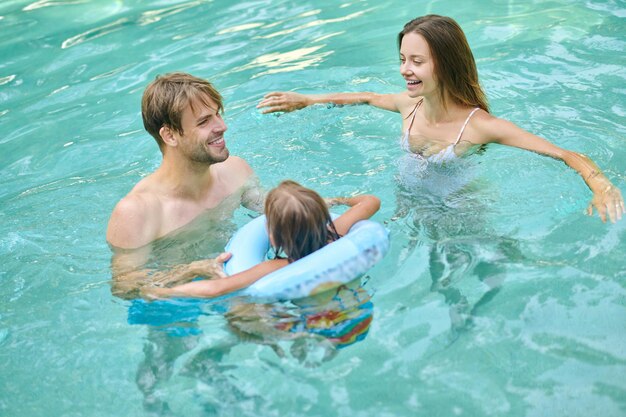 At the swimming pool. Parents teaching theri daughter to swim and looking involved