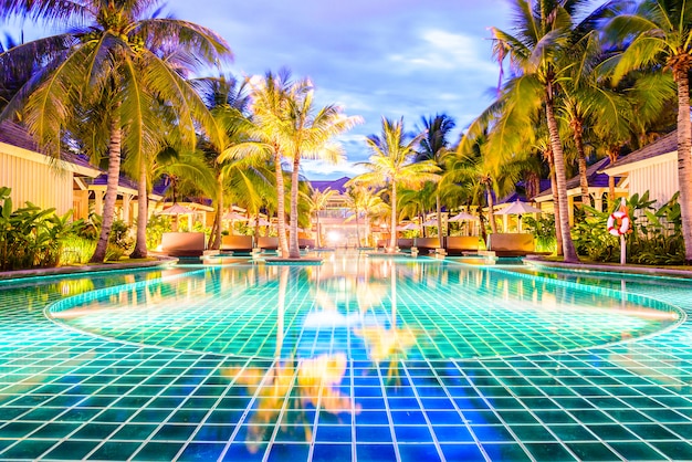 Free photo swimming pool with palm trees in resort hotel at night