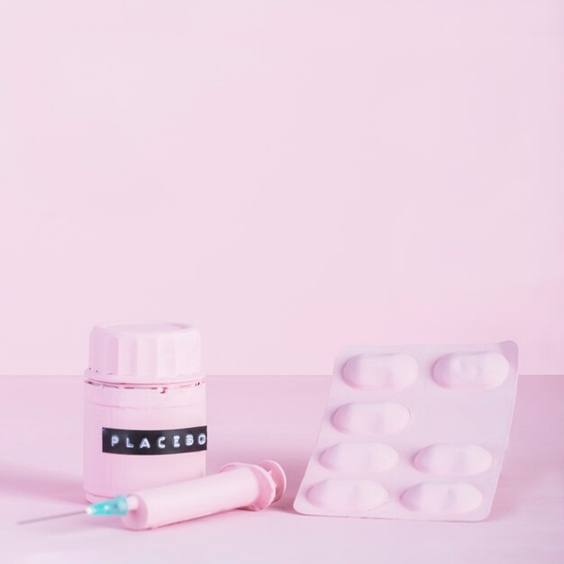 Syringe, pill blister and placebo bottle on pink background