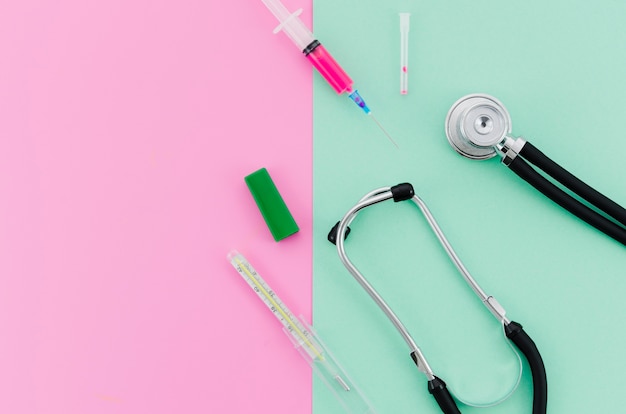 Free photo syringe; stethoscope; thermometer on pink and mint green background