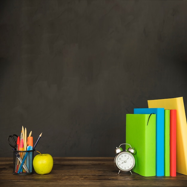 Table with textbooks alarm clock stationery and apple