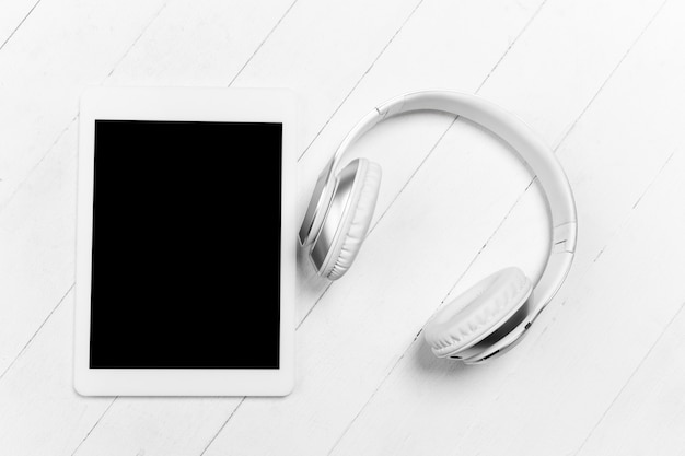 Tablet and headphones. Blank screen. Monochrome stylish and trendy composition in white color on studio wall. Top view, flat lay.