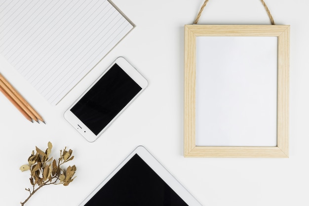 Tablet near smartphone, paper, pencils and photo frame