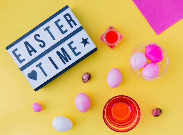 Free photo tablet with easter time title near eggs between cans with dye liquid and napkin