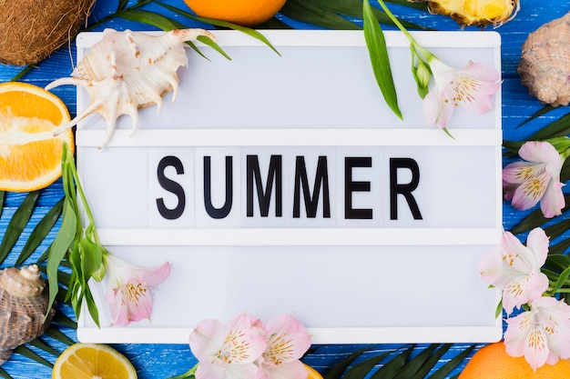 Tablet with summer word among plant leaves near flowers and fruits