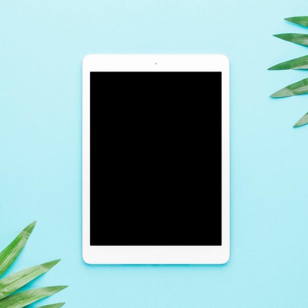 Free photo tablet with tropical leaves on light background