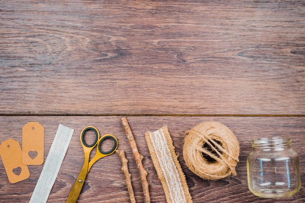 Free photo tags; ribbon; scissor; sticks; jute spool and an empty transparent jar on wooden desk