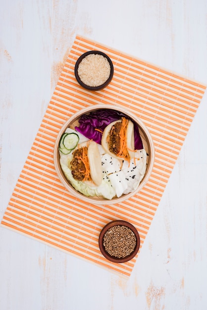 Free photo taiwan's traditional food gua bao steamed sandwich on steamer with bowls of rice and coriander seeds over the placemat