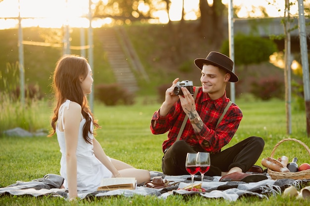 Taking photo. Caucasian young couple enjoying weekend together in the park on summer day. Look lovely, happy, cheerful. Concept of love, relationship, wellness, lifestyle. Sincere emotions.