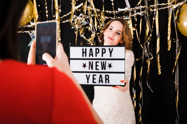 Taking photo of girl holding happy new year sign