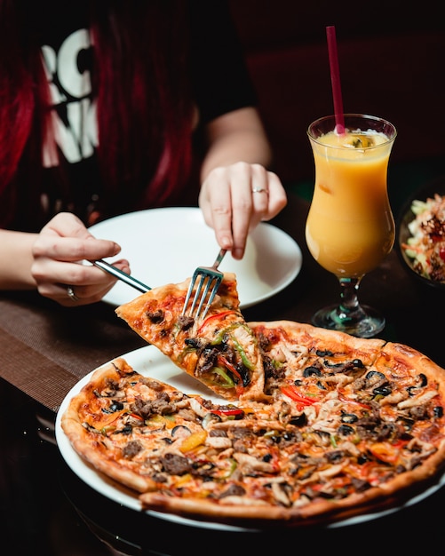 Free photo taking a slice of mixed ingredient pizza with a glass of orange juice.