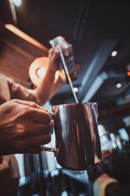 Talanted barista is pouring milk to the jug for latte or cappuchino at his cafe.