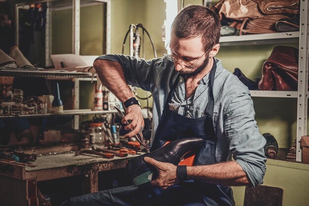 Talented cobbler is working on pair of black men's shoes at his workshop.