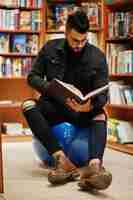 Free photo tall smart arab student man wear on black jeans jacket and eyeglasses sitting at library and read book at hands