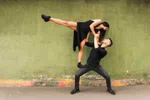 Free photo tango male dancer carrying woman in black dress on his lap