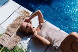 Free photo tanned fit caucasian woman in shiny short dress lying near blue swimming pool