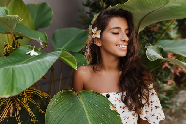 Free Photo tanned long-haired woman in white top with floral print enjoying summer day on vacation in warm country