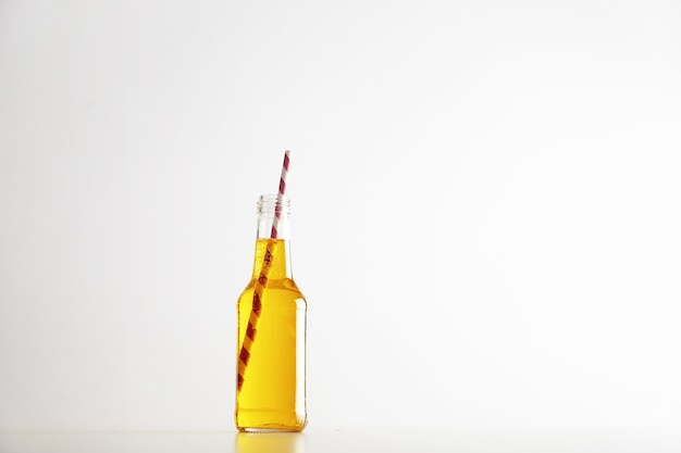 Tastu sparkling yellow drink with red striped drinking straw inside opened rustic glass bottle isolated on white