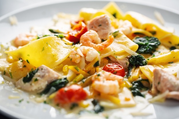 Tasty appetizing pasta with shrimps, vegetables and spinach served on plate.