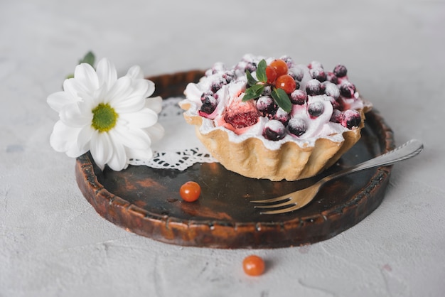 Tasty berries tart with fork and flower on round wooden tray