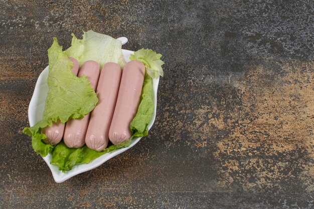 Tasty boiled sausages and lettuce on leaf shaped plate.