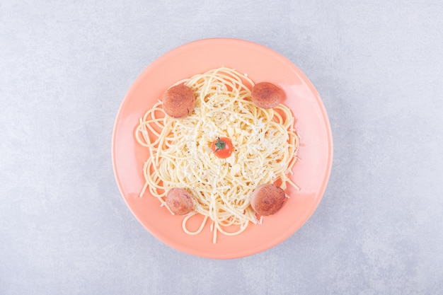 Tasty boiled spaghetti with sausages on orange plate. 