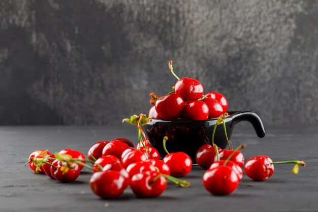 Tasty cherries in a black scoop on grungy and grey table, side view.