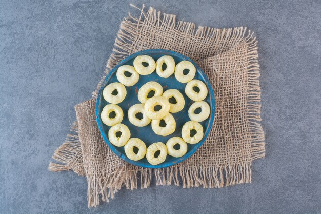 Tasty corn rings on a wooden plate on texture, on the marble surface.