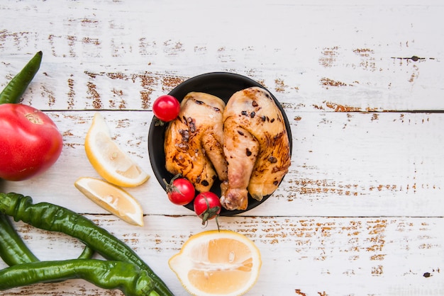 Free Photo tasty delicious roasted chicken in bowl with lemon; tomato; green chilies on wooden desk