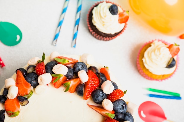 Tasty fresh cake with berries on table near ornament balloons