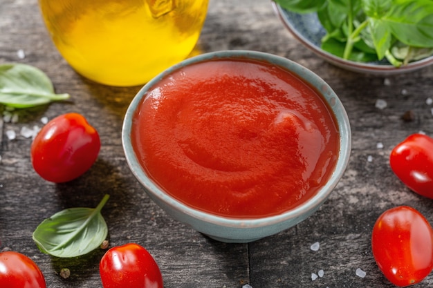 Free photo tasty fresh tomato sauce in small bowl with ingredients for cooking on old wooden background. closeup