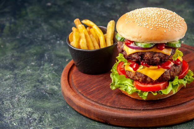 Tasty homemade sandwich fries on wooden cutting board on the right side on dark color surface