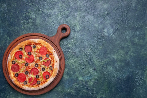 Tasty pizza on wooden cutting board on the right side on dark blue surface with free space