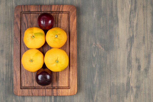 Tasty plums with delicious tangerines on a wooden plate