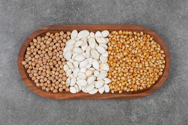 Tasty pumpkin seeds, corn kernels and peas on wooden plate.