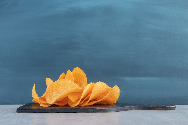 Tasty spicy potato chips on black cutting board.